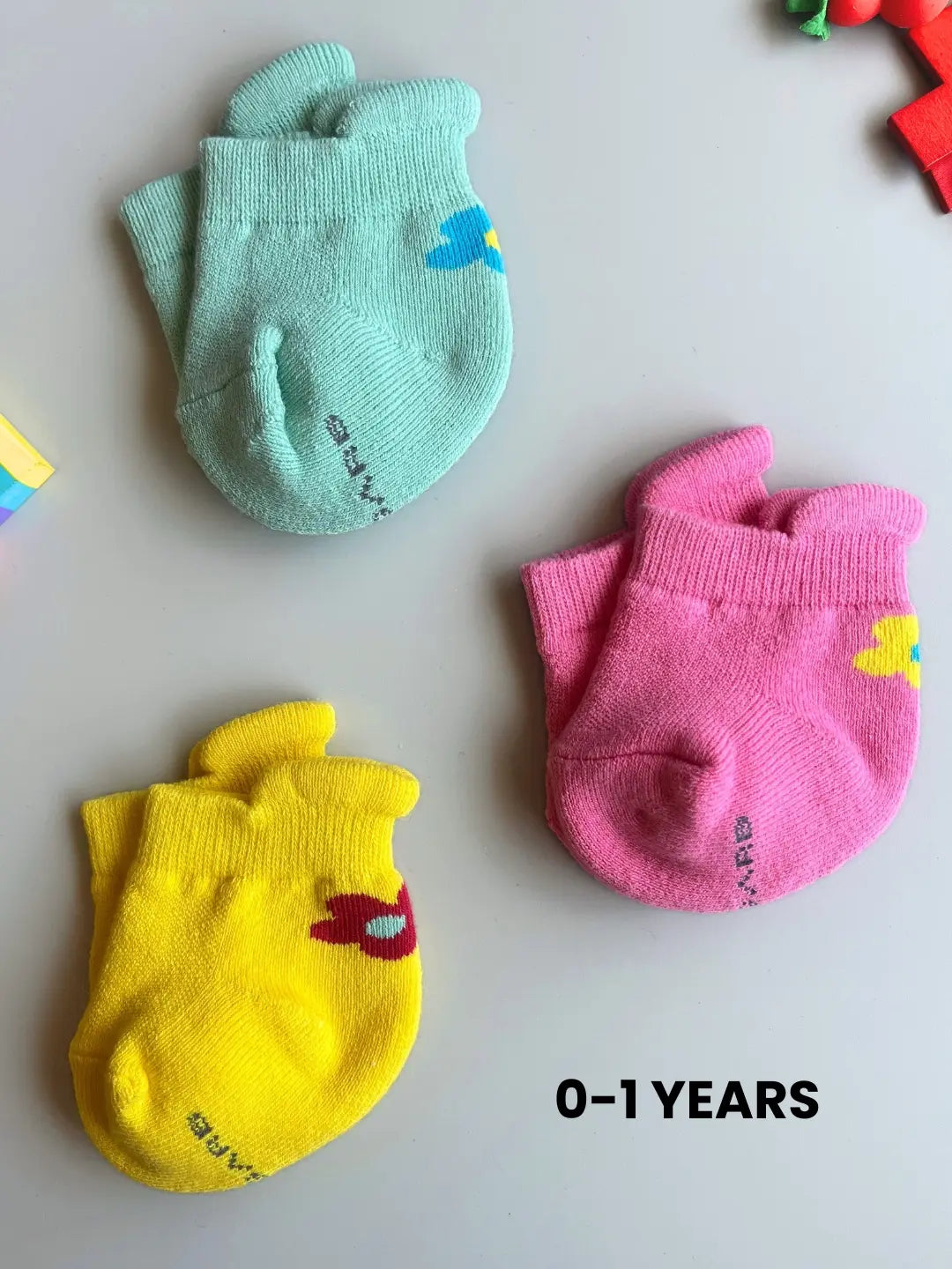 Air Garb brand baby combo socks for infants 0-1 years; a 6-pair collection arranged in a circle featuring three pairs with side flower designs (pink, yellow, mint) and three pairs with kitten face cuffs (purple, lime green, blue).