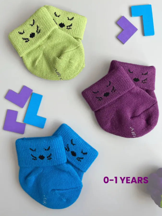 Air Garb brand baby combo socks for infants 0-1 years; a 6-pair collection arranged in a circle featuring three pairs with side flower designs (pink, yellow, mint) and three pairs with kitten face cuffs (purple, lime green, blue).